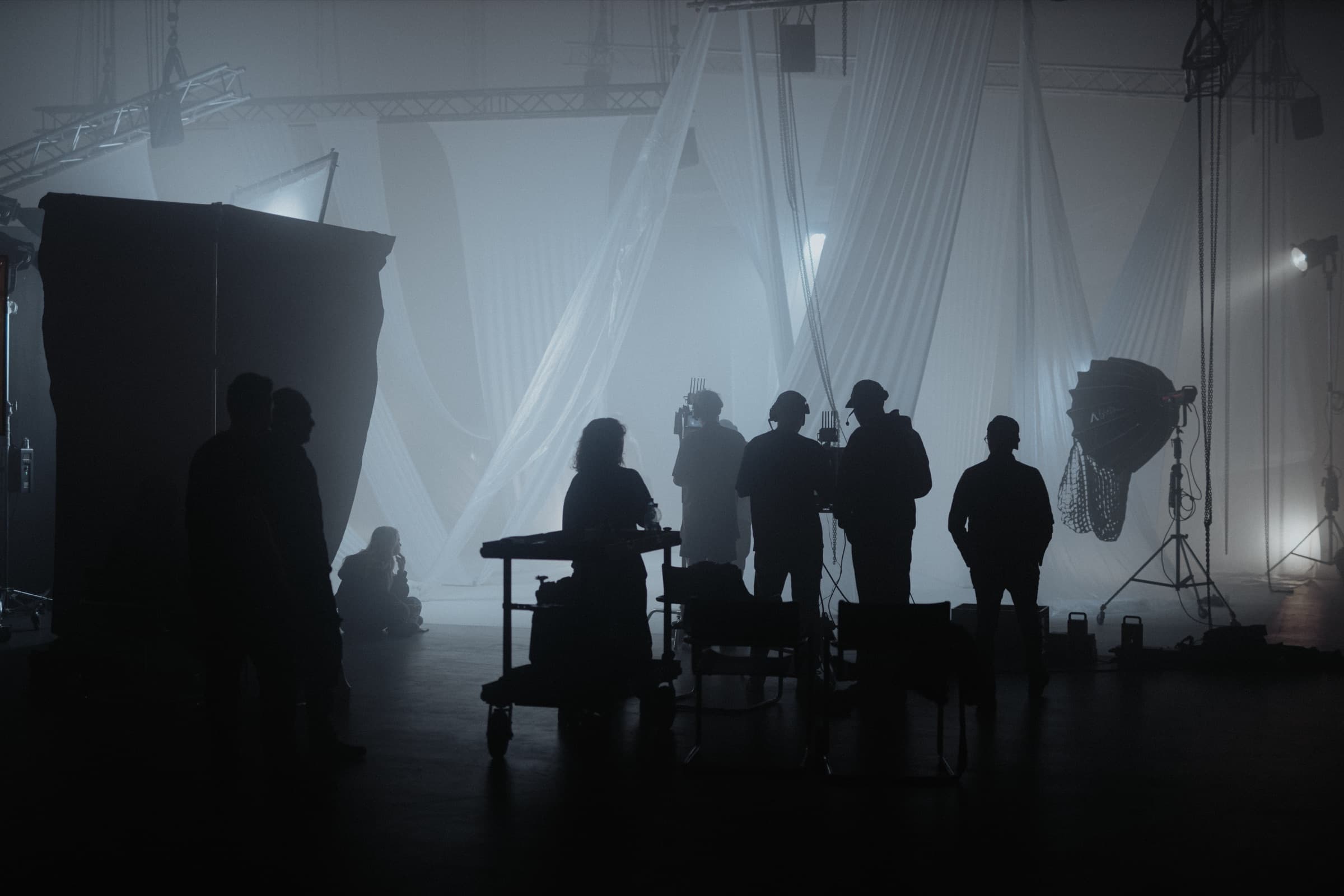 Filmset im Studio: Crew im Gegenlicht vor weißen Stoffbahnen